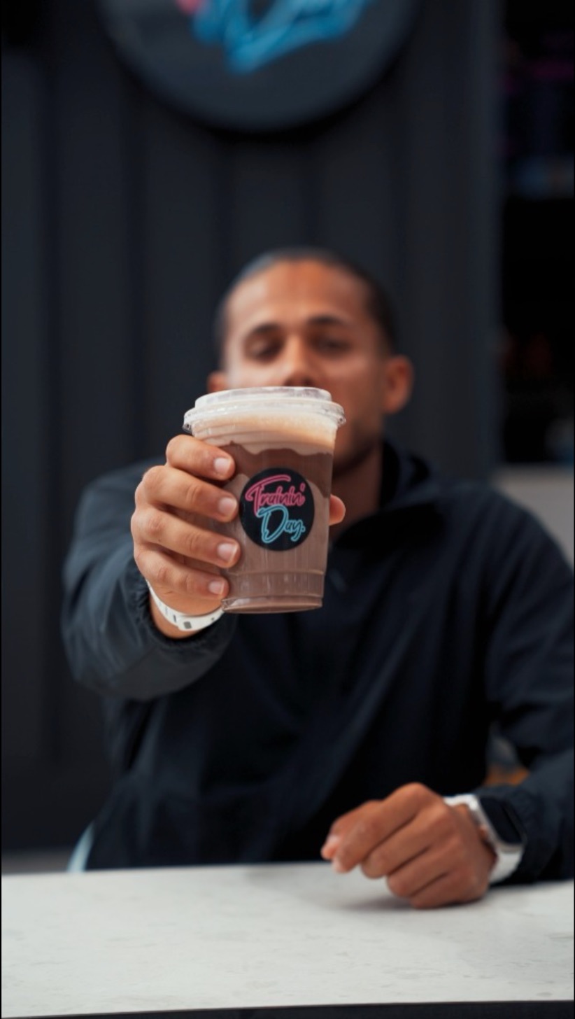 An iced chocolate in a Trainin Day branded cup, held out across the counter